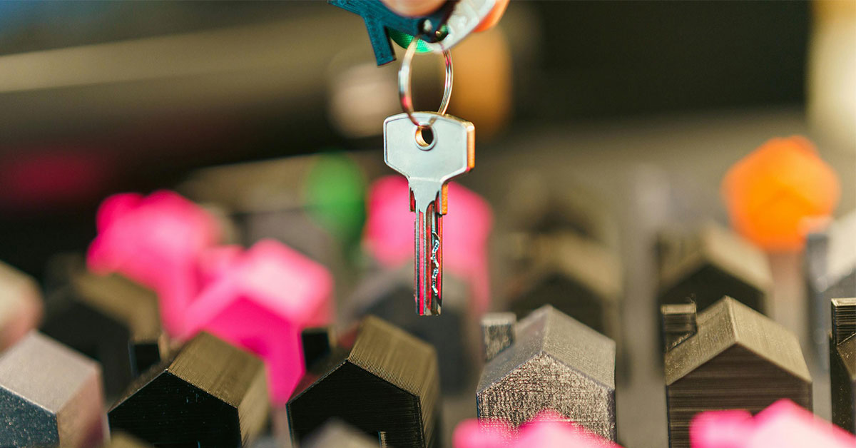 Key hanging over small plastic houses that are brown, silver, and pink.